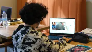 Teenager, der einen Laptop zum Lernen zu Hause nutzt, umgeben von Lernmaterialien und Büchern.