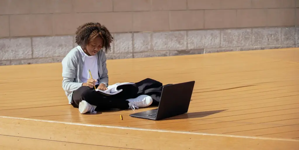 Fokussiertes Teenager-Mädchen, das draußen studiert, mit einem Laptop und einem Notizbuch im natürlichen Licht.