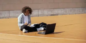 Fokussiertes Teenager-Mädchen, das draußen studiert, mit einem Laptop und einem Notizbuch im natürlichen Licht.
